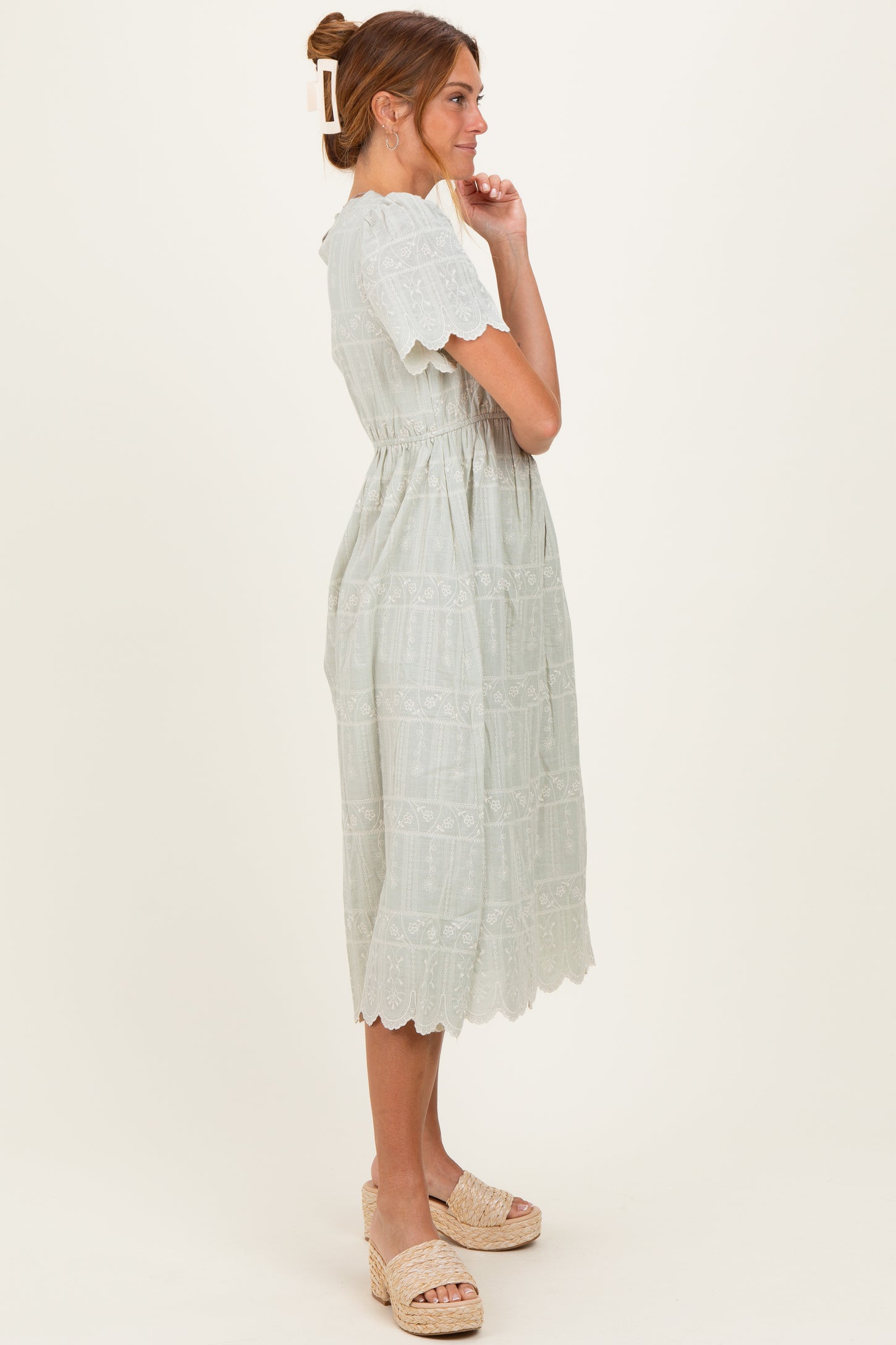 woman wearing a light green midi dress with lace detailing and puff sleeves, standing sideways with a relaxed pose