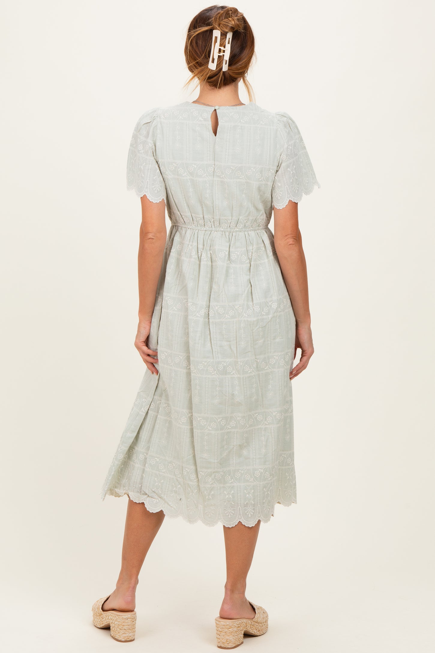 woman wearing a light green midi dress with short sleeves and lace detailing, showing a back keyhole and elastic waist