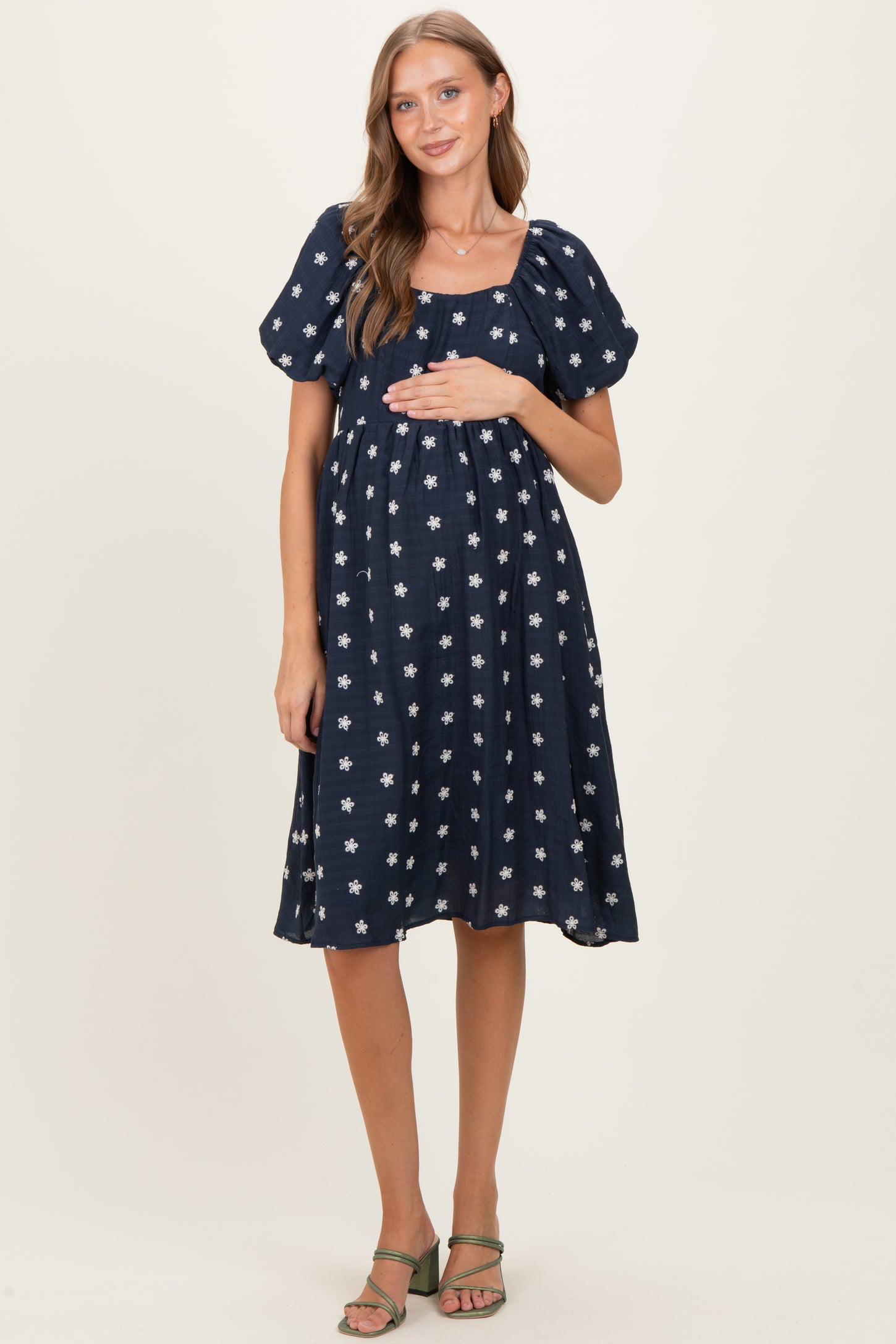woman wearing a navy blue maternity dress with white floral print and puff sleeves, highlighting her baby bump