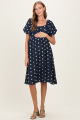 woman wearing a navy blue maternity dress with white floral print and puff sleeves, highlighting her baby bump