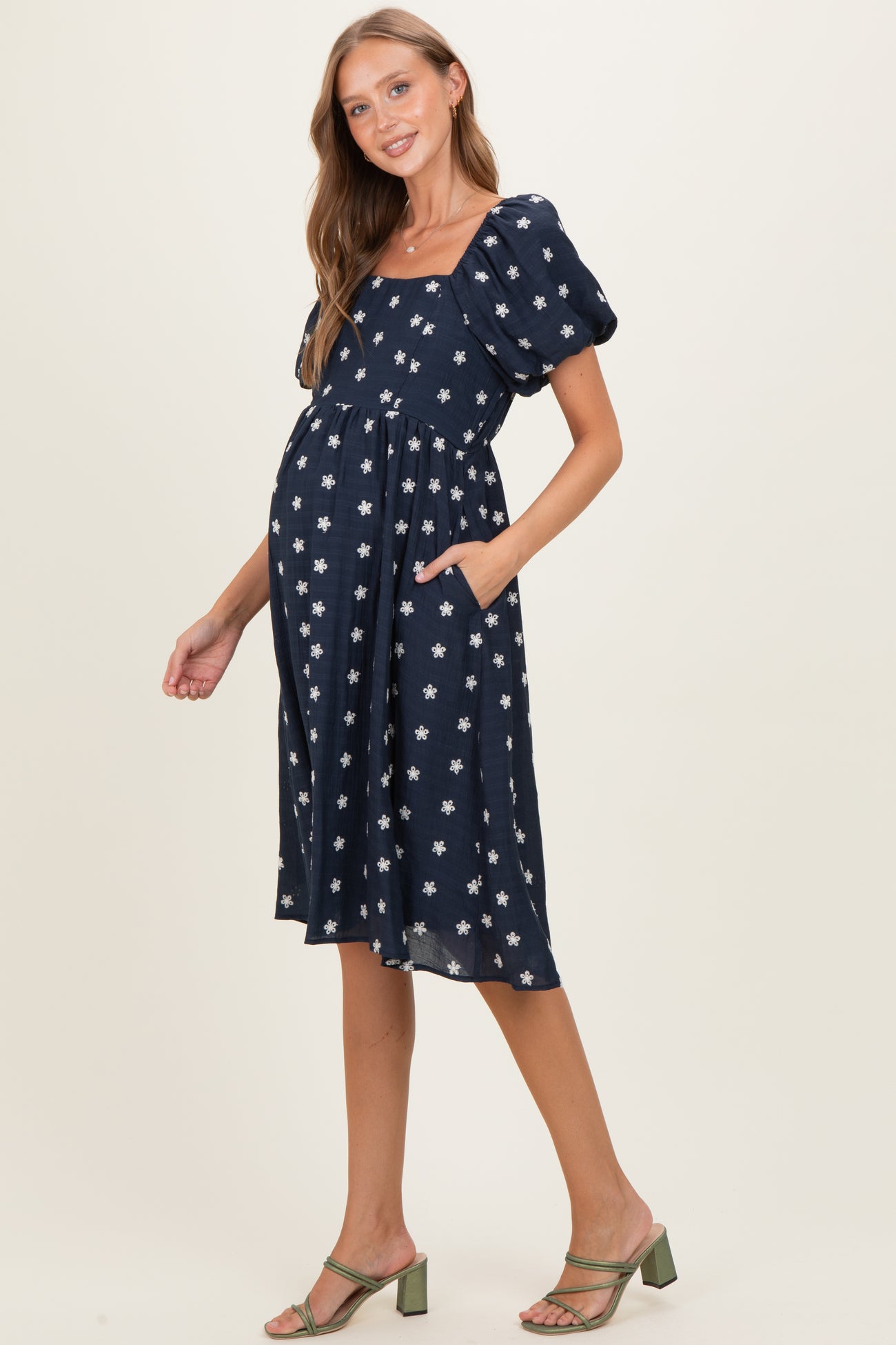 woman wearing a navy blue maternity dress with puff sleeves and white floral print, showing her baby bump