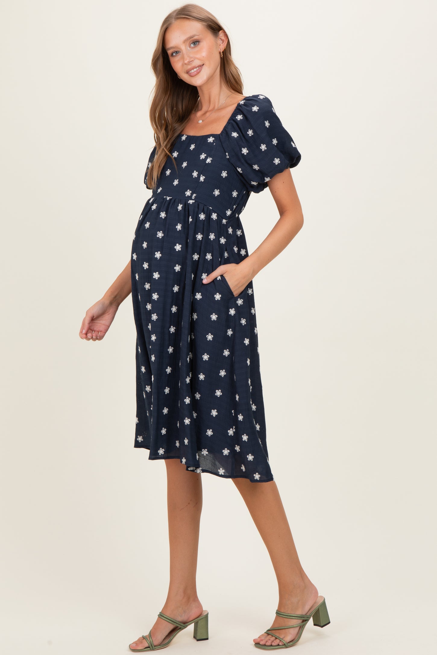 woman wearing a navy blue maternity dress with puff sleeves and white floral print, showing her baby bump