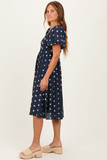 woman wearing a navy blue midi dress with white floral print and short puff sleeves, standing sideways