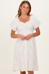 woman wearing a white puff sleeve dress with a square neckline and floral texture