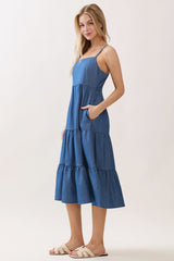 woman wearing a blue tiered chambray midi dress with spaghetti straps and pockets