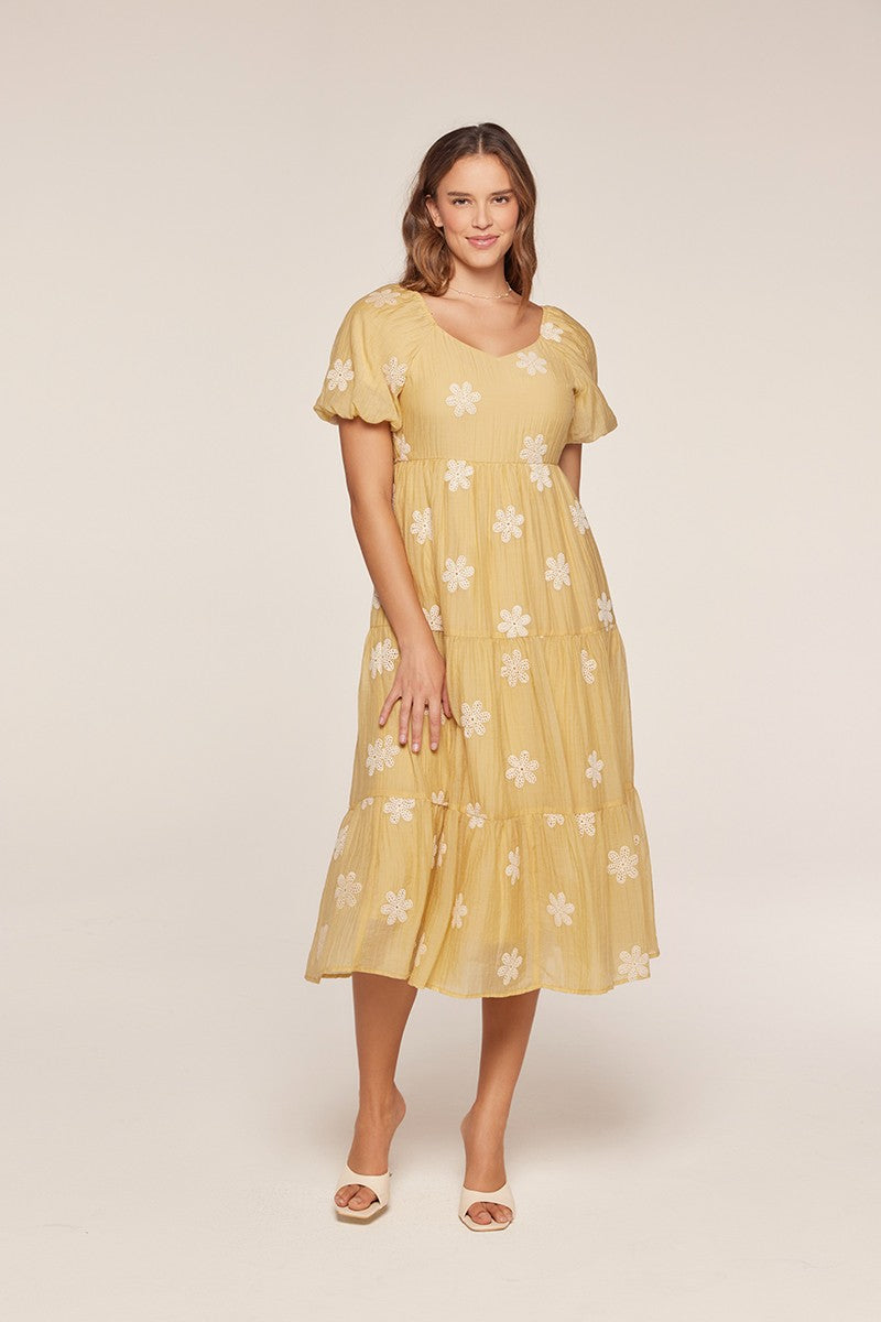 woman wearing a yellow tiered midi dress with white floral embroidery and short puff sleeves
