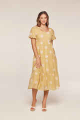 woman wearing a yellow tiered midi dress with white floral embroidery and short puff sleeves