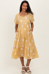 woman wearing a yellow maternity dress with puff sleeves and white floral embroidery, featuring pockets and a tiered skirt
