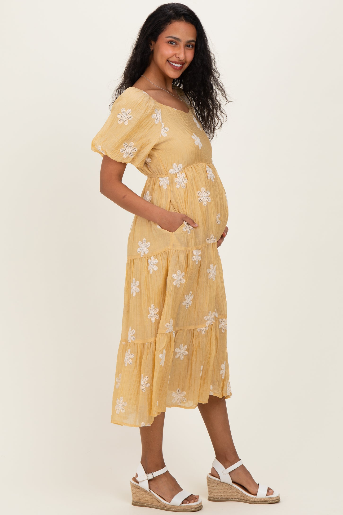 woman wearing a yellow floral maternity dress with pockets and a baby bump, standing sideways