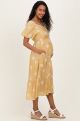 woman wearing a yellow floral maternity dress with pockets and a baby bump, standing sideways