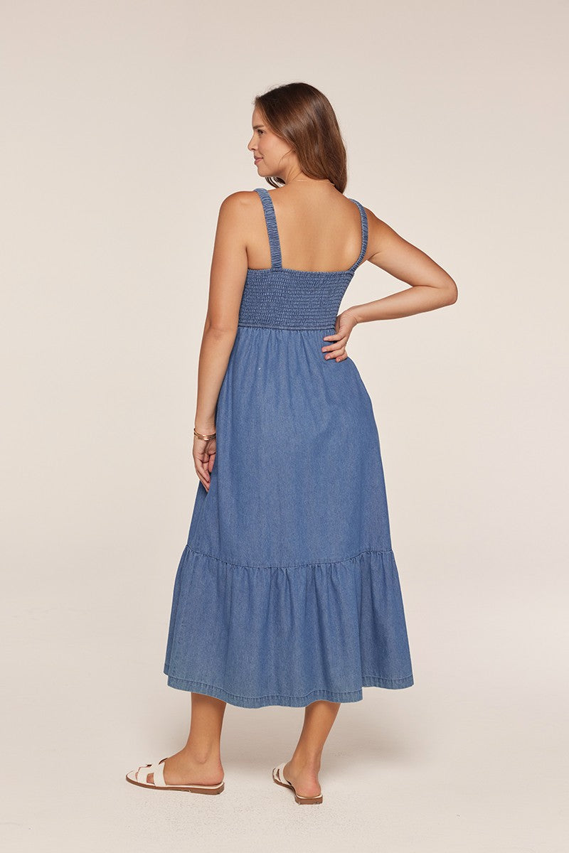 woman wearing a blue denim maxi dress with smocked bodice and tiered skirt, shown from the back