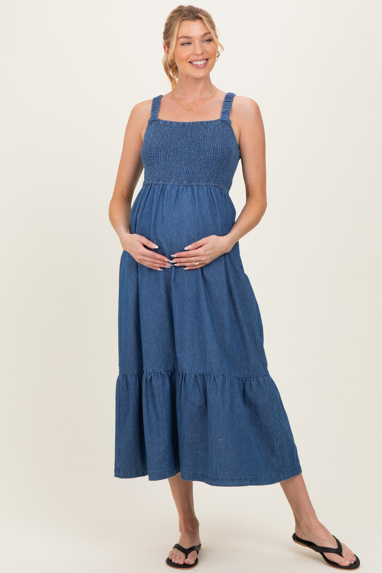 woman wearing a dark denim maternity maxi dress with smocked bodice and tiered skirt, holding her baby bump