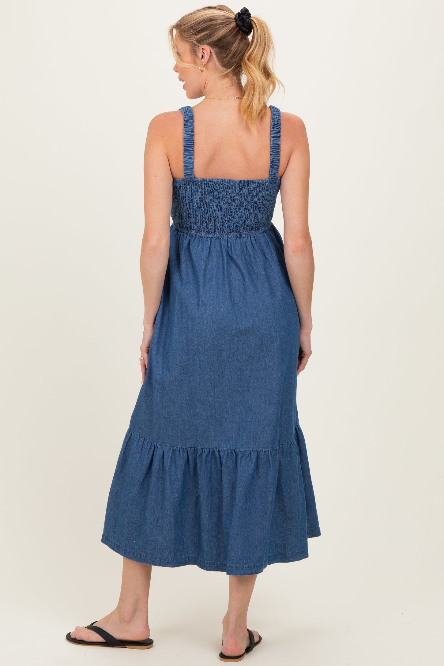 woman wearing a denim blue maternity maxi dress with smocked bodice and tiered ruffle hem, showing her baby bump from the back