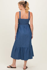 woman wearing a denim blue maternity maxi dress with smocked bodice and tiered ruffle hem, showing her baby bump from the back