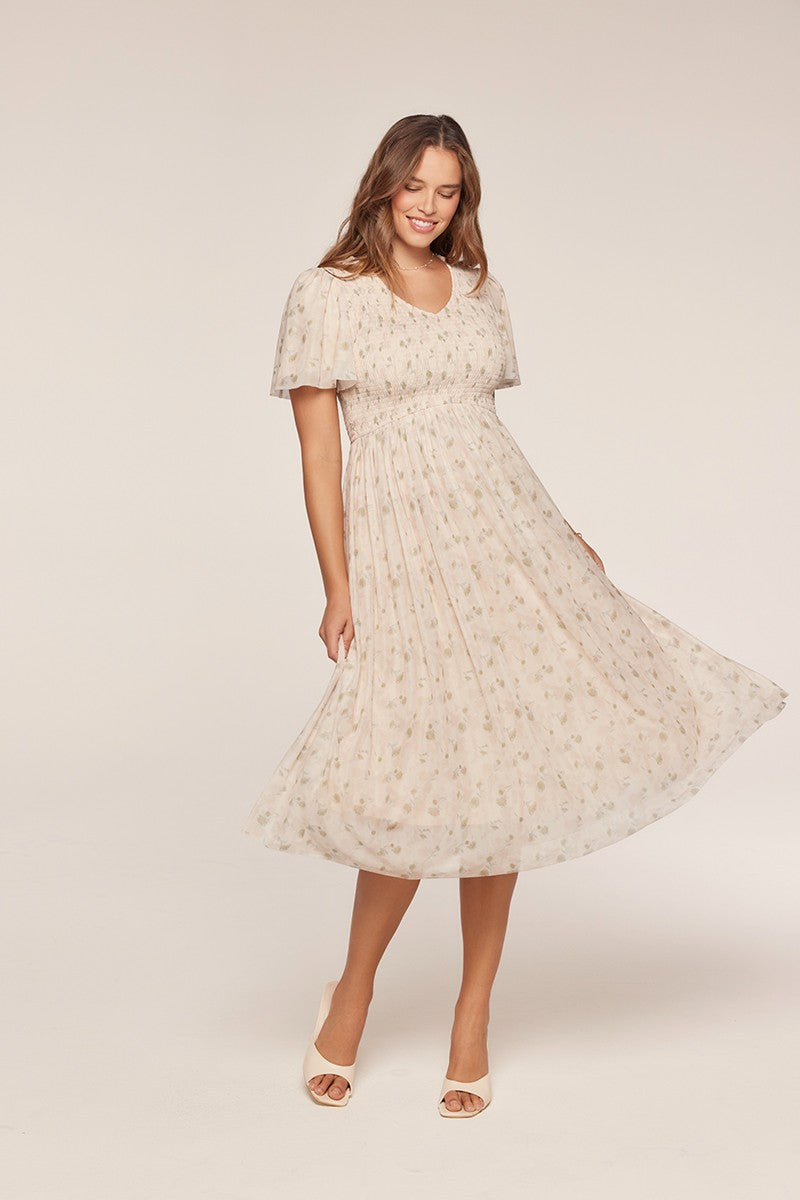 woman wearing a cream floral midi dress with a smocked bodice and flutter sleeves, spinning gracefully