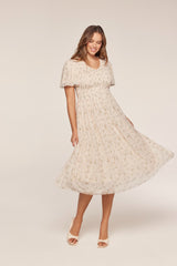 woman wearing a cream floral midi dress with a smocked bodice and flutter sleeves, spinning gracefully