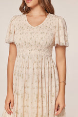 woman wearing a floral print smocked dress with short flutter sleeves and a v-neckline