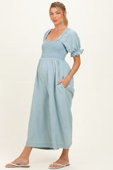 woman wearing a light blue maternity dress with a smocked bodice and puff sleeves, showing her baby bump and pockets