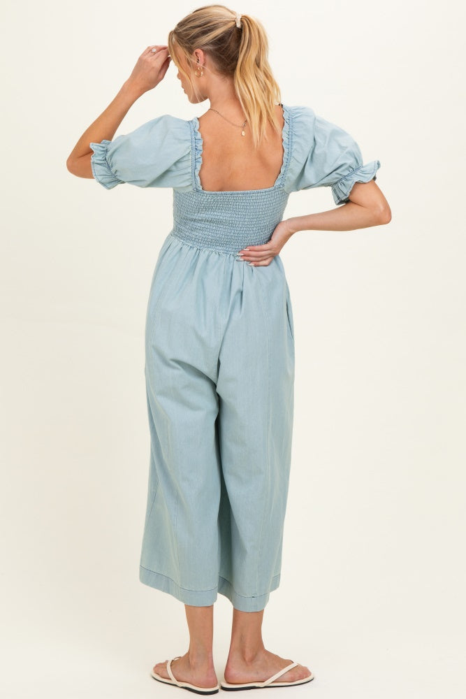 woman wearing a light blue maternity jumpsuit with puff sleeves and a smocked back, standing and looking to the side