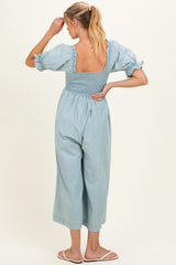 woman wearing a light blue maternity jumpsuit with puff sleeves and a smocked back, standing and looking to the side