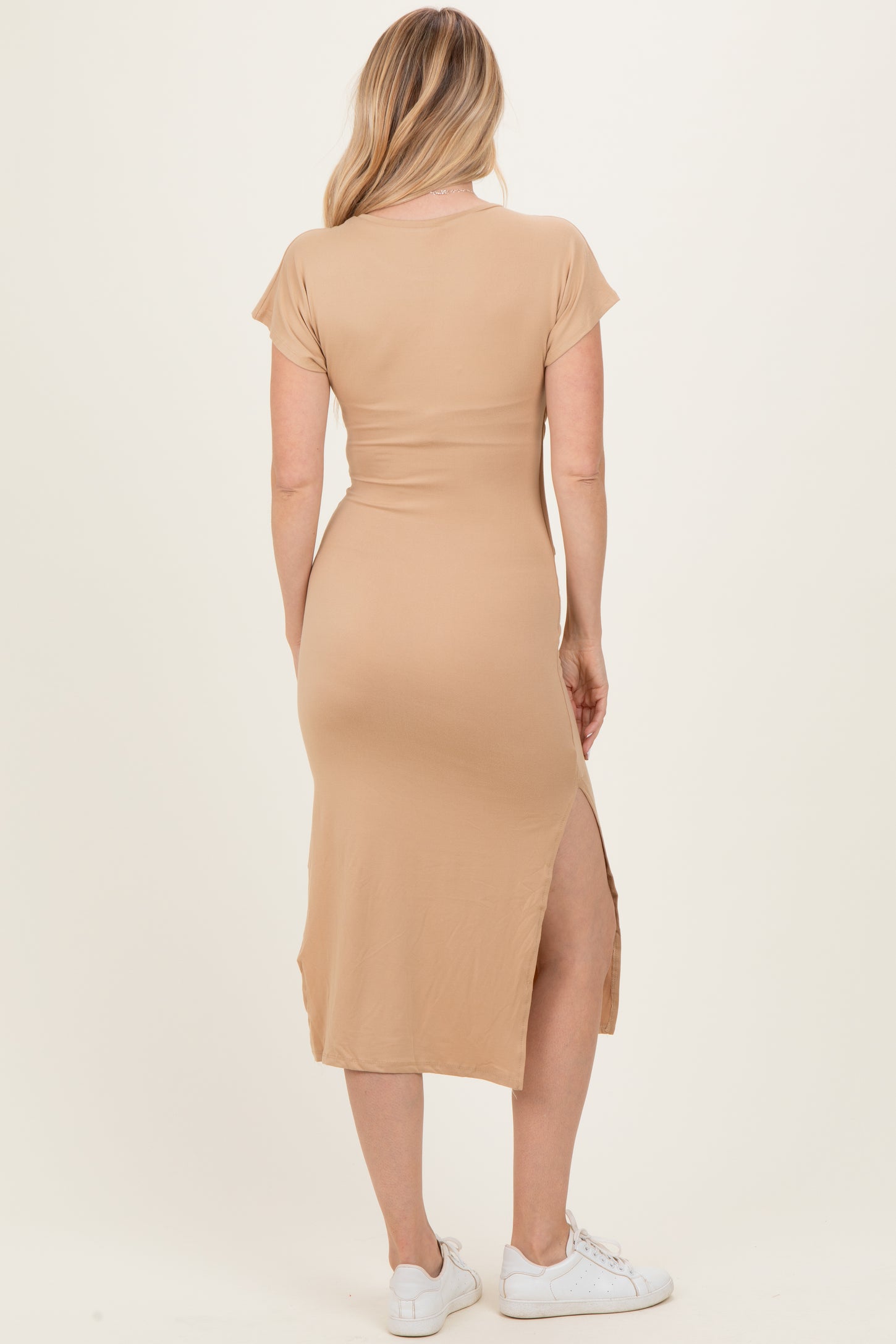 woman wearing a tan short sleeve maxi dress with a side slit, showing the back view and styled with white sneakers