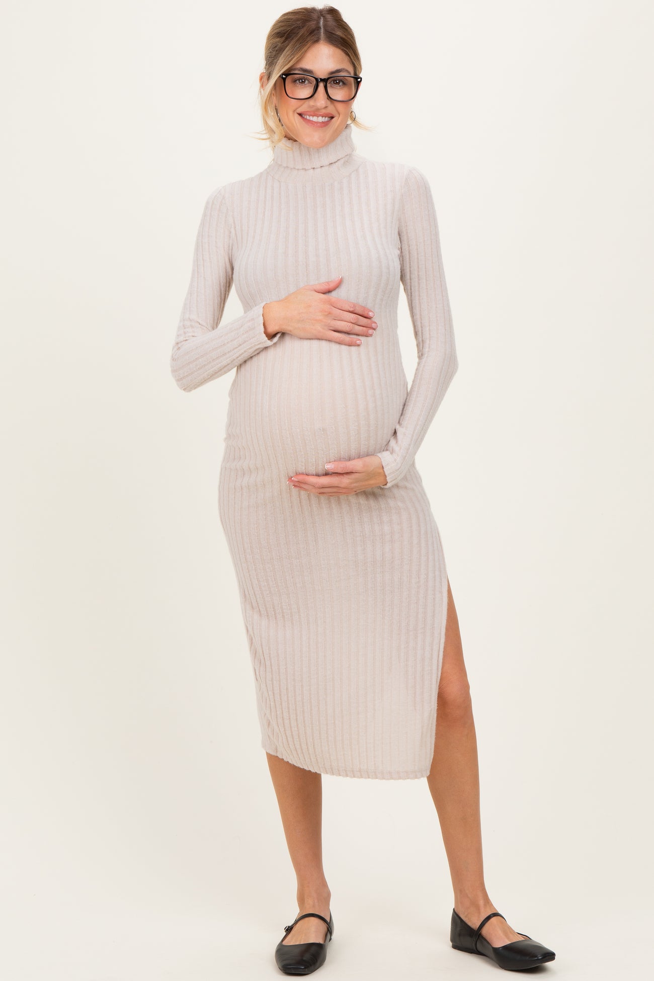 woman wearing a beige ribbed maternity dress with a high neckline and side slit, holding her baby bump