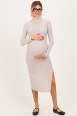 woman wearing a beige ribbed maternity dress with a high neckline and side slit, holding her baby bump