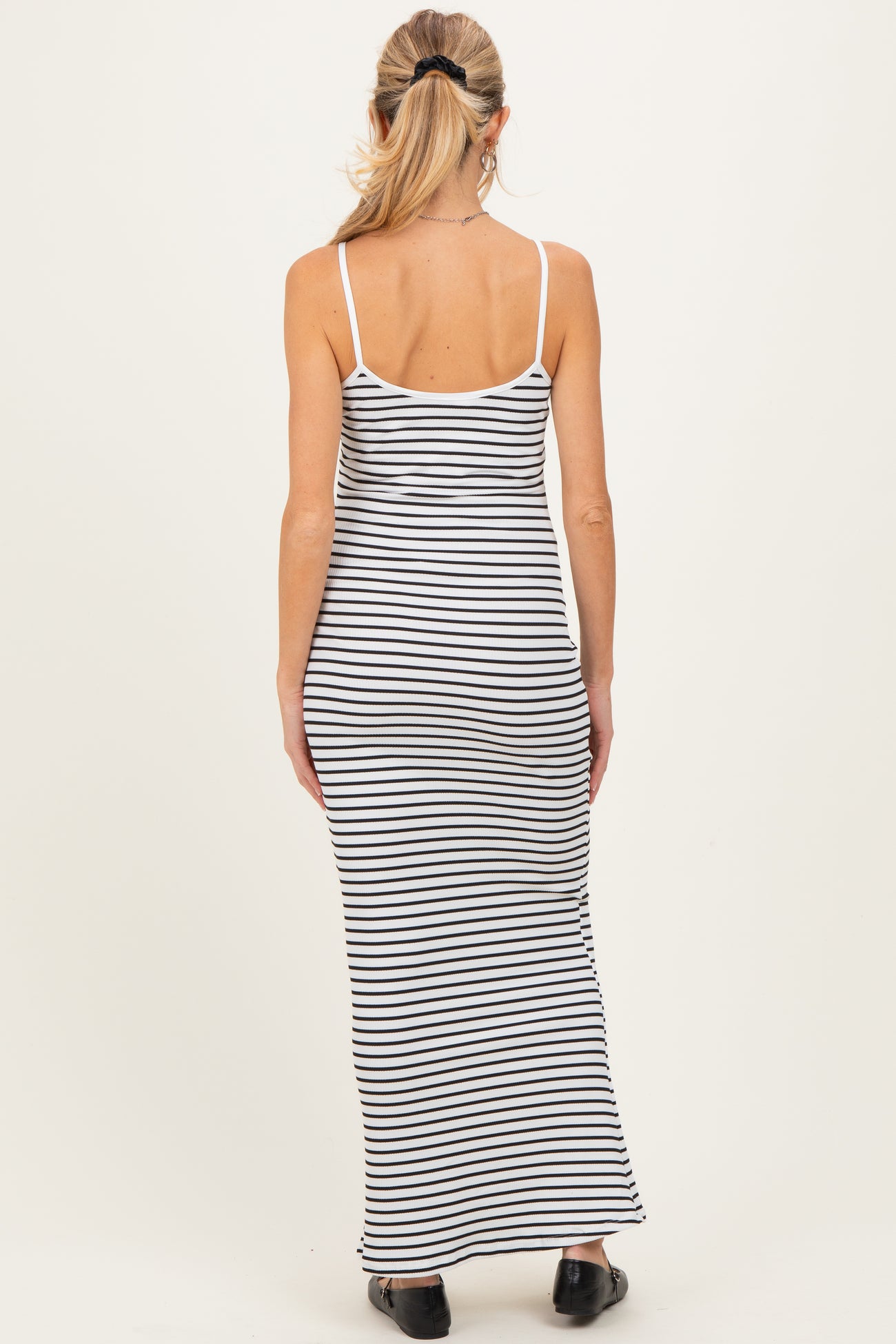 woman wearing a black and white striped maternity maxi dress with spaghetti straps, showcasing a fitted silhouette