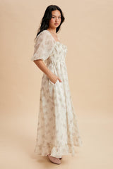 woman wearing a white floral maxi dress with short puff sleeves and pockets, standing against a beige background