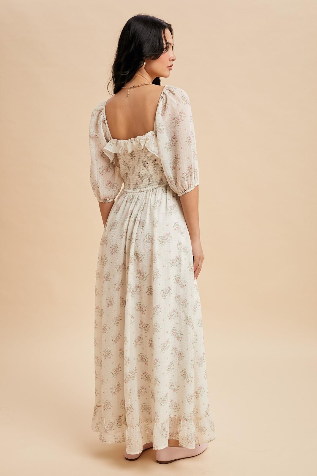 woman wearing a flowy cream floral maxi dress with puff sleeves and a ruffled back detail