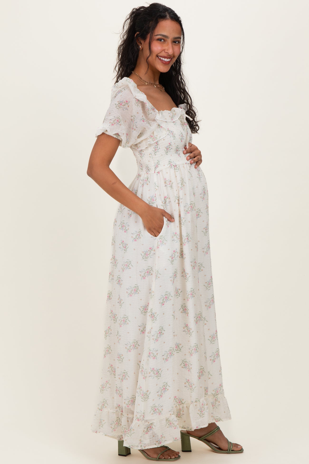 woman wearing a white floral maternity dress with short sleeves and a ruffled neckline, holding her baby bump