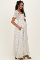 woman wearing a white floral maternity dress with short sleeves and a ruffled neckline, holding her baby bump