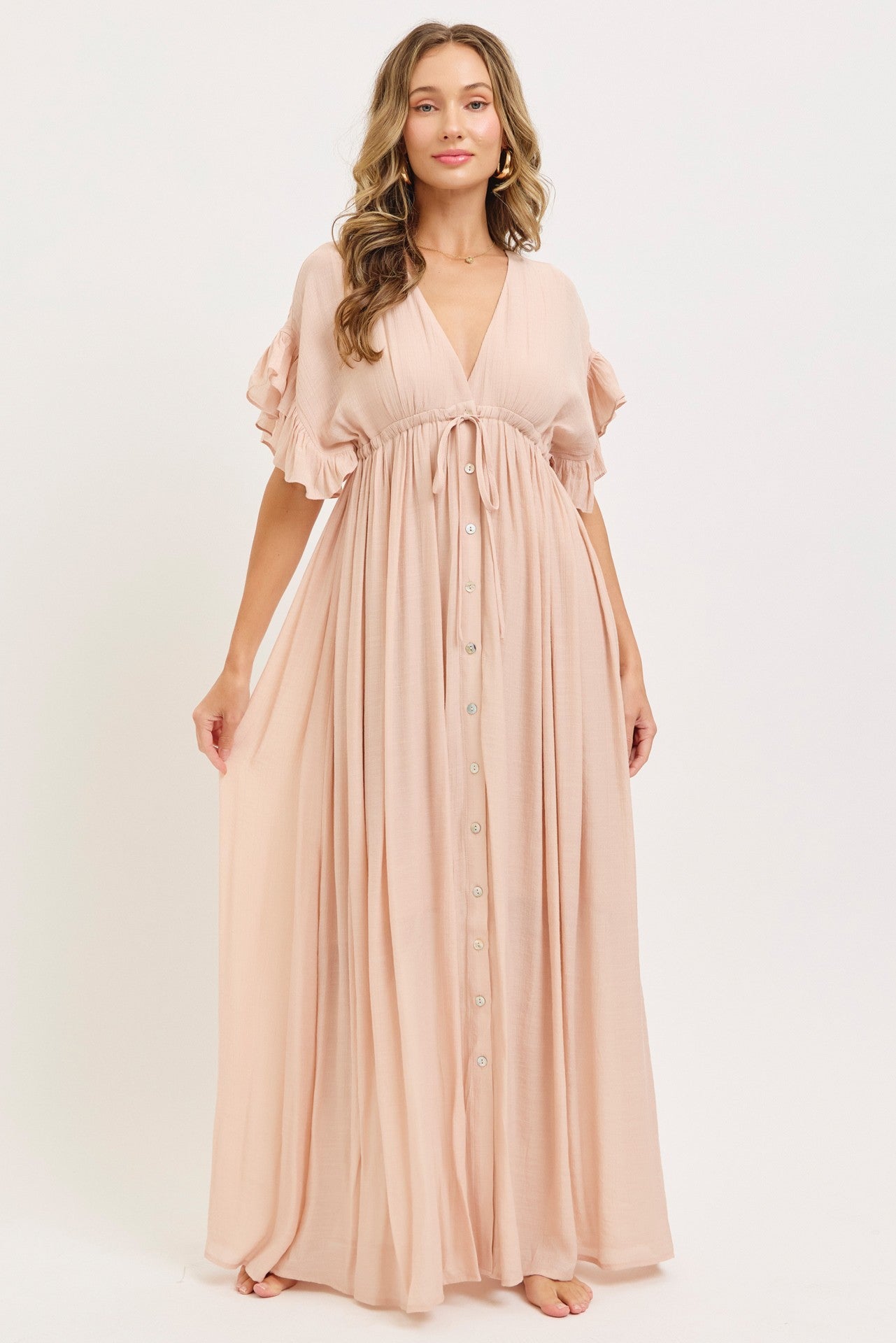 woman wearing a blush pink maxi dress with ruffled sleeves and a tie-front detail, standing barefoot