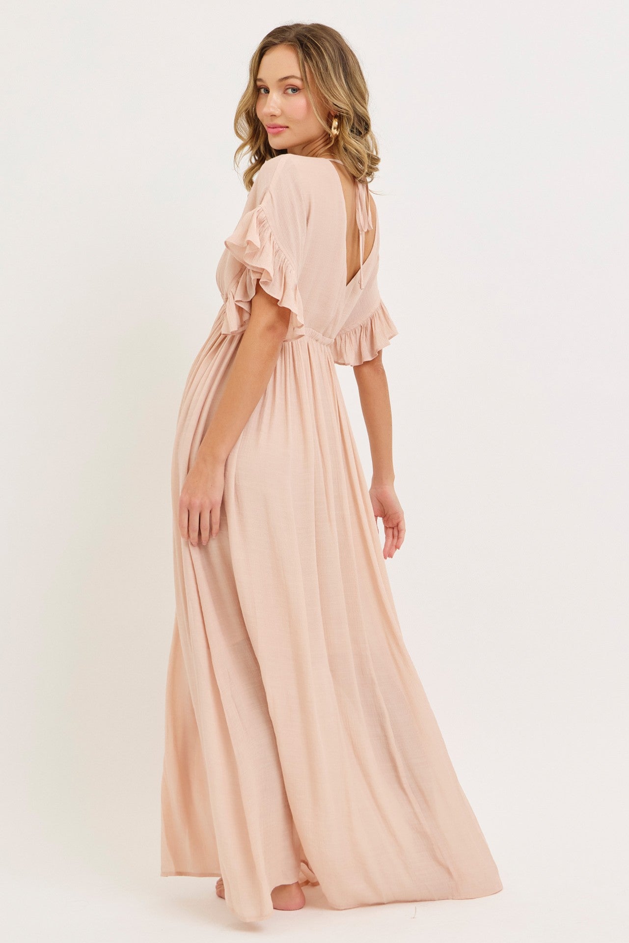 woman wearing a light pink maxi dress with ruffle sleeves and a low back, shown from the back