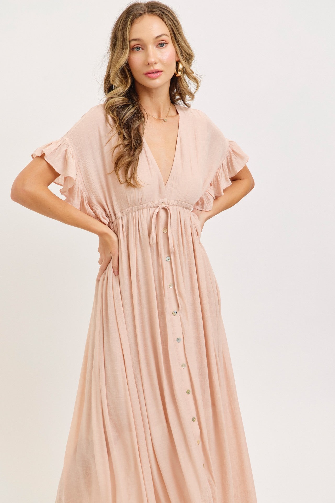 woman wearing a blush pink maxi dress with ruffled sleeves and a button-down front