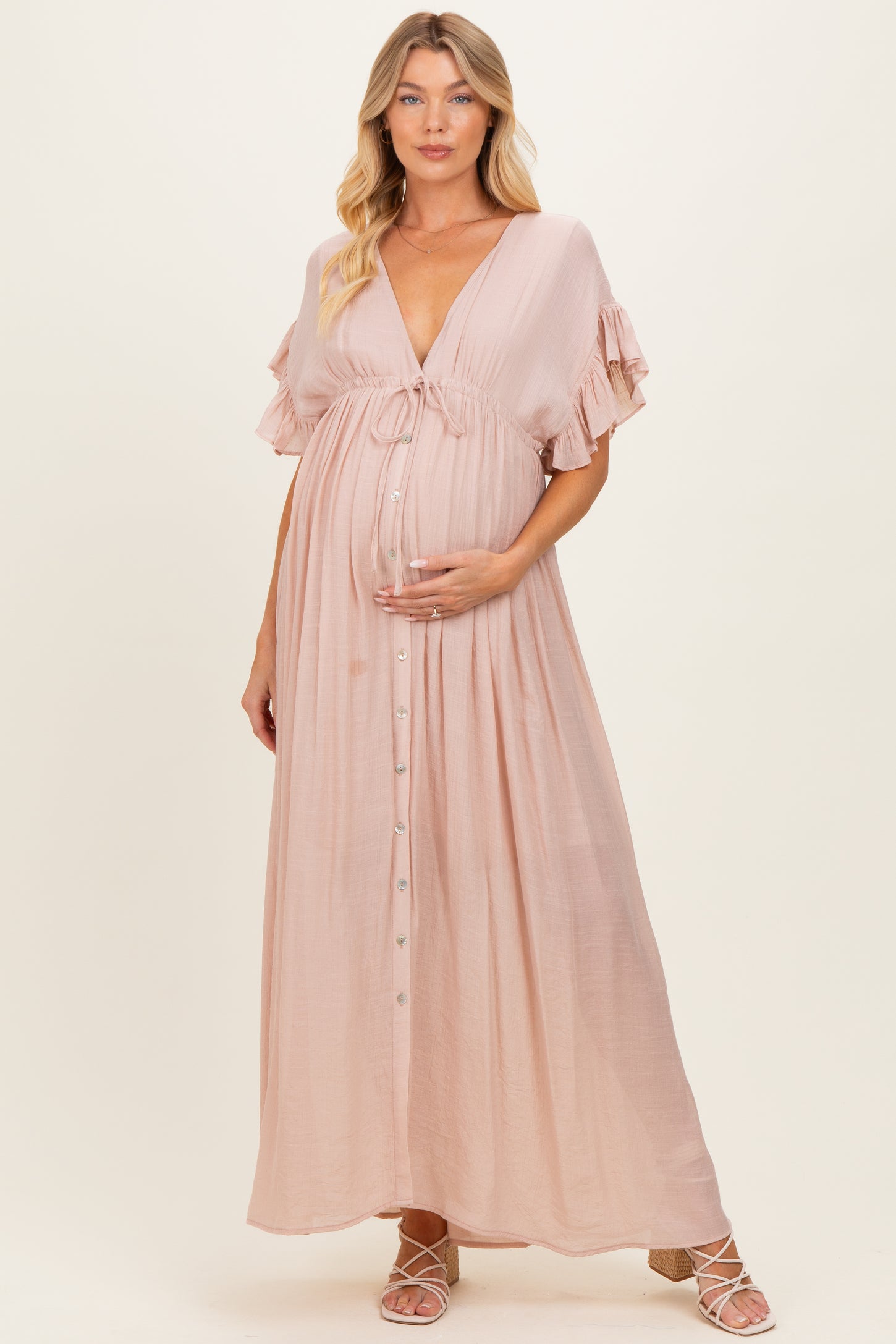 woman wearing a blush pink maternity maxi dress with ruffled sleeves and a button front, holding her baby bump