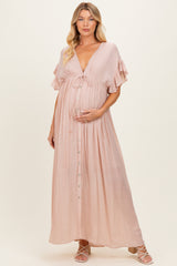 woman wearing a blush pink maternity maxi dress with ruffled sleeves and a button front, holding her baby bump