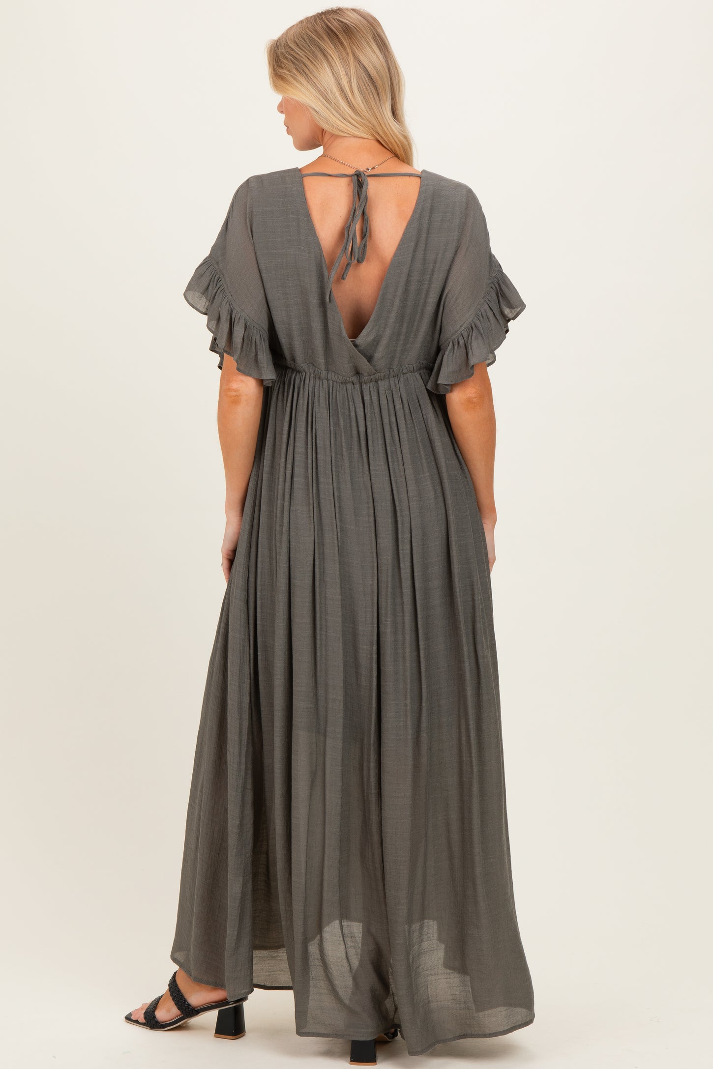 woman wearing a grey maternity maxi dress with ruffle sleeves and an open back, styled for comfort during pregnancy