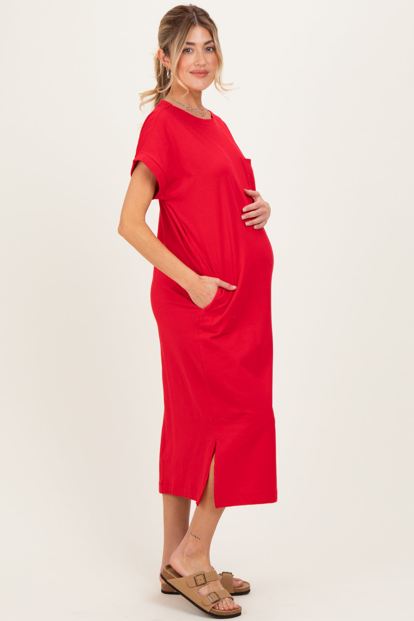 woman wearing a red maternity dress with pockets and a side slit, gently holding her baby bump
