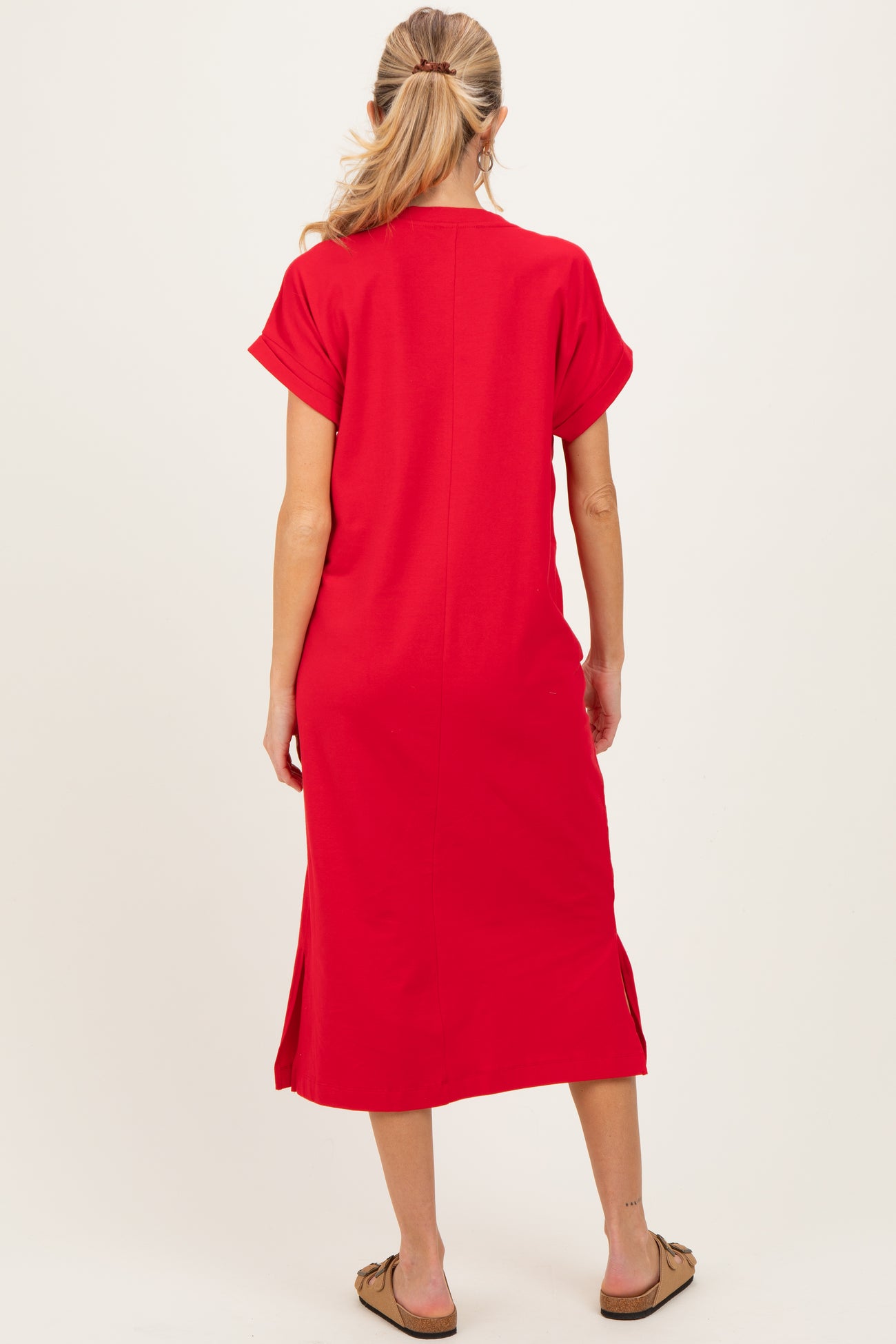 woman wearing a red maternity maxi dress with short sleeves and side slits, standing with her back to the camera