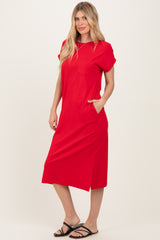 woman wearing a red short sleeve midi dress with a pocket and side slit, standing with hands in pockets