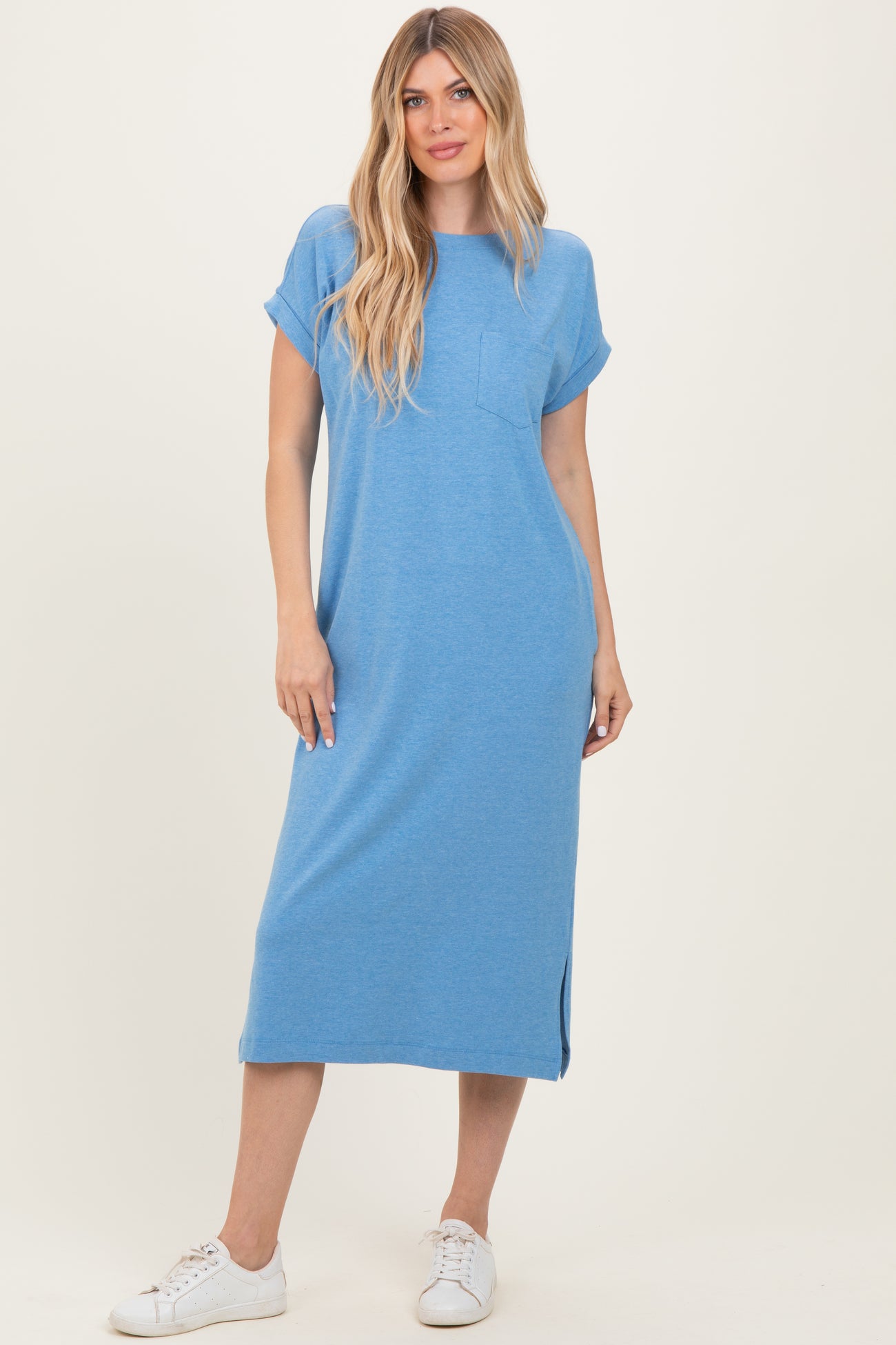 woman wearing a blue short sleeve midi dress with a pocket and side slits, paired with white sneakers