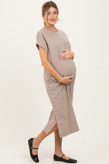 woman wearing a taupe maternity dress with short sleeves and side slits, gently holding her baby bump