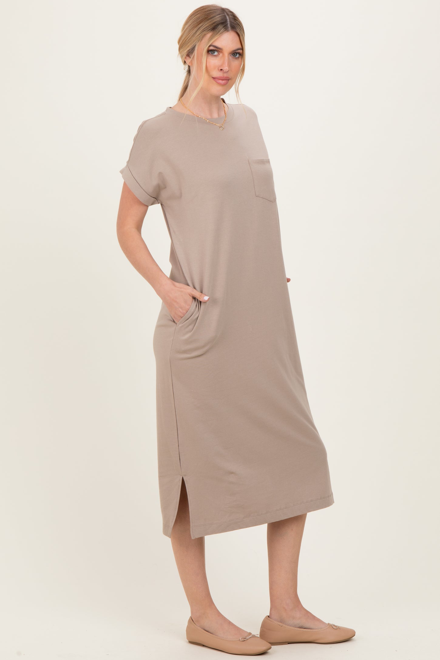 woman wearing a beige short sleeve midi dress with a pocket and side slits, standing with hands in pockets