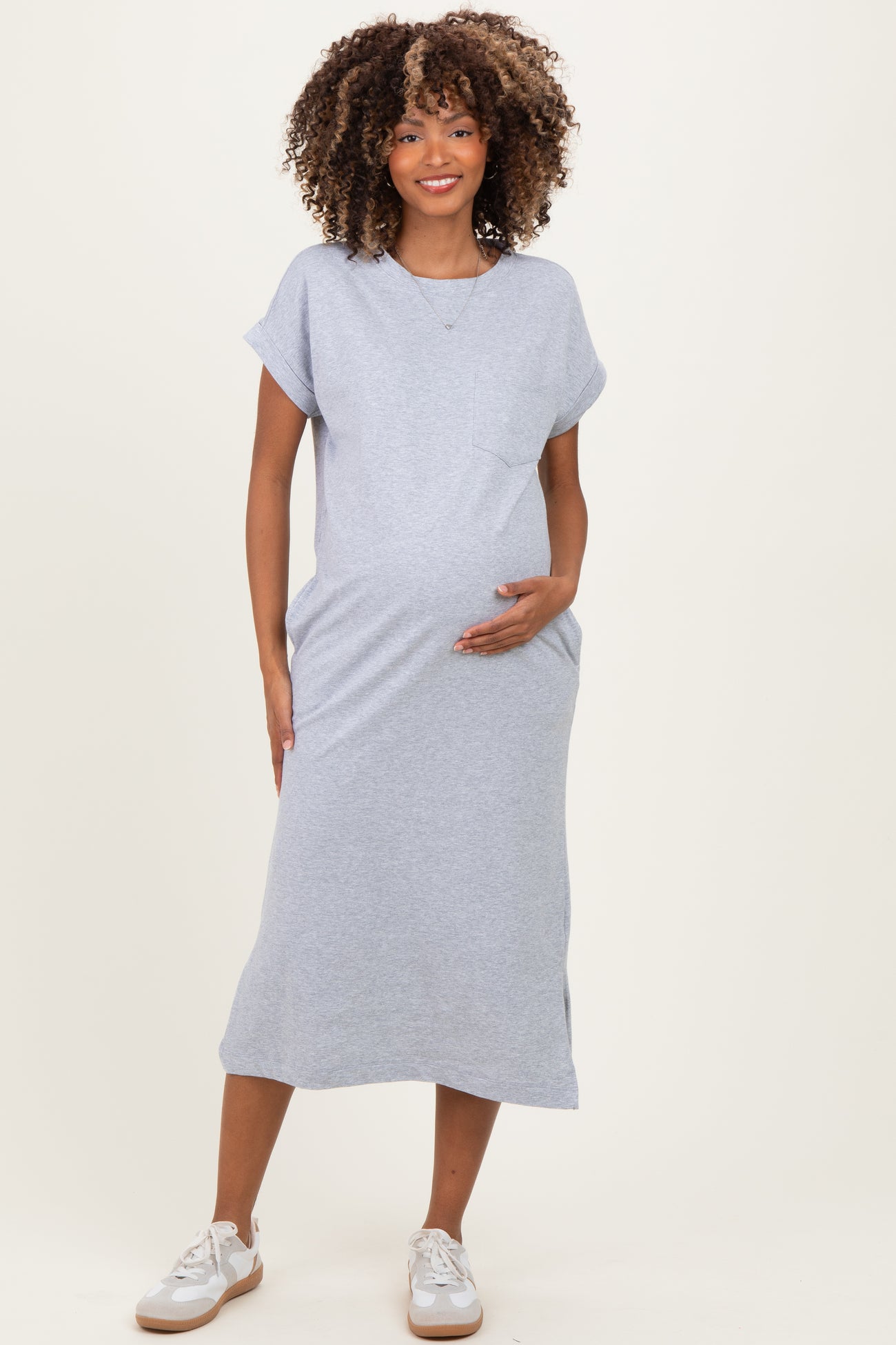 woman wearing a gray short sleeve maternity dress with a pocket and holding her baby bump