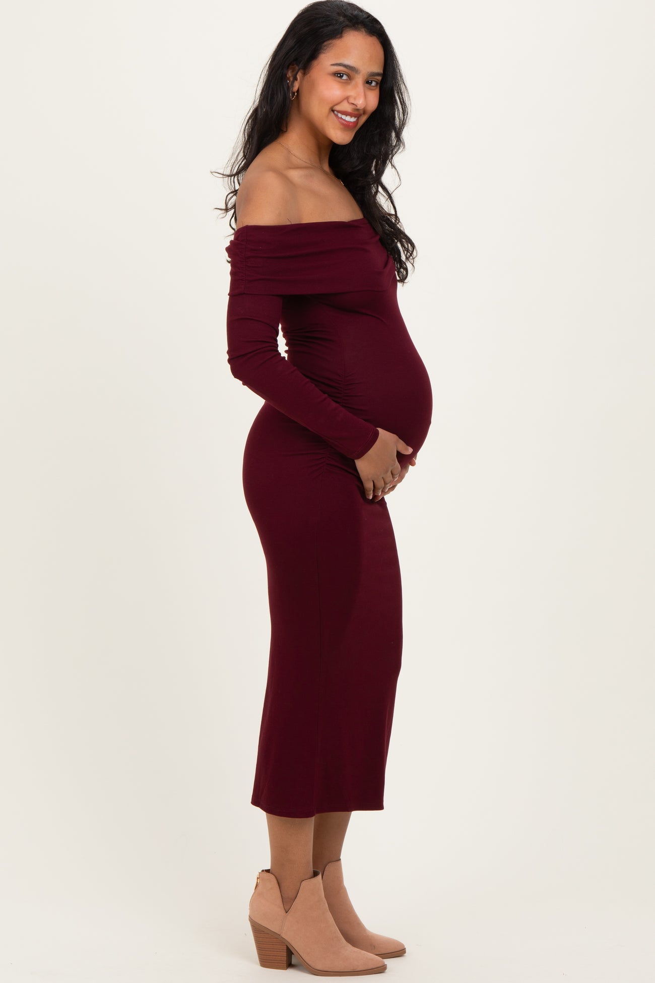 woman wearing a burgundy off-shoulder maternity dress showing her baby bump