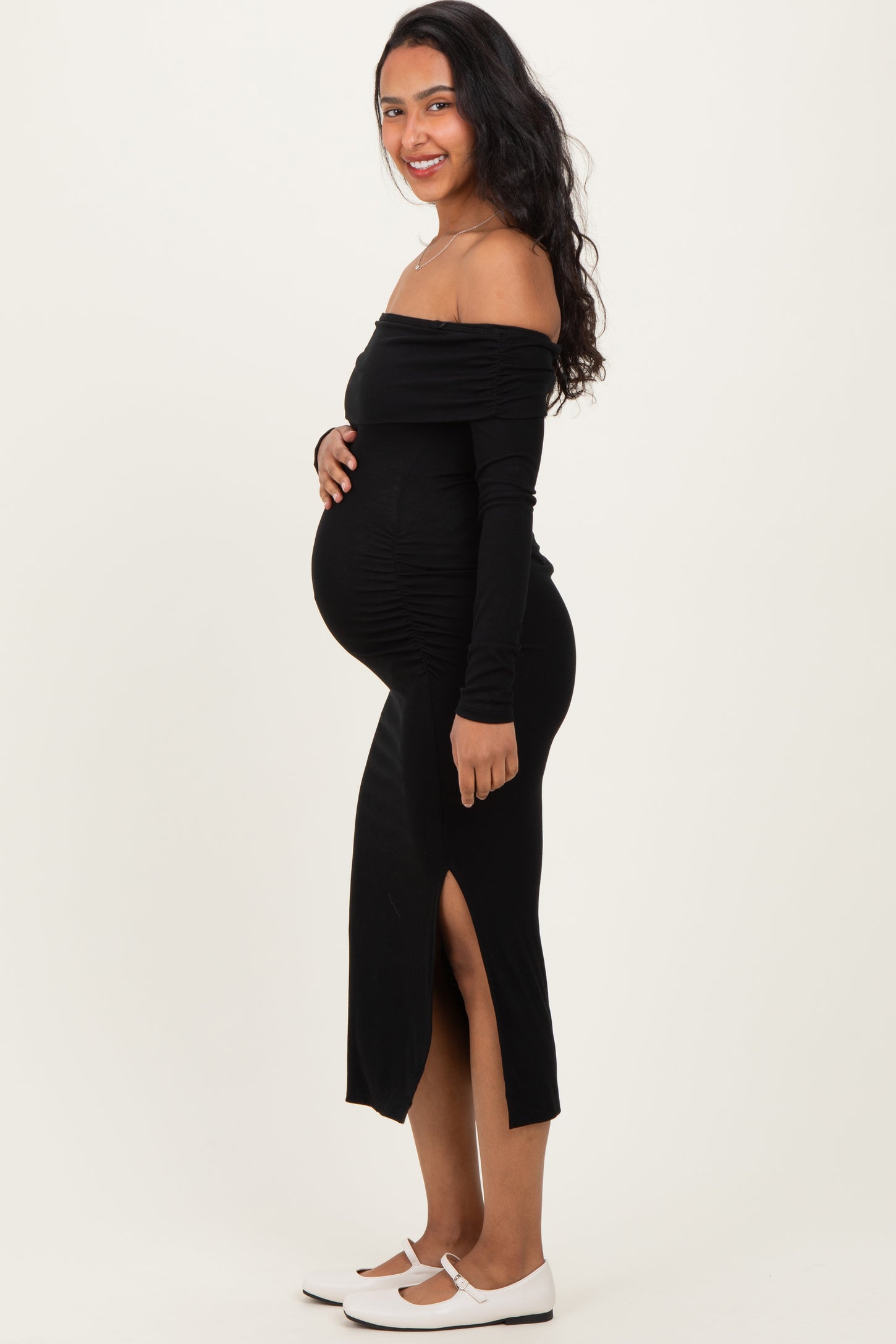 woman wearing a black off-the-shoulder maternity dress with side slit and showing her baby bump