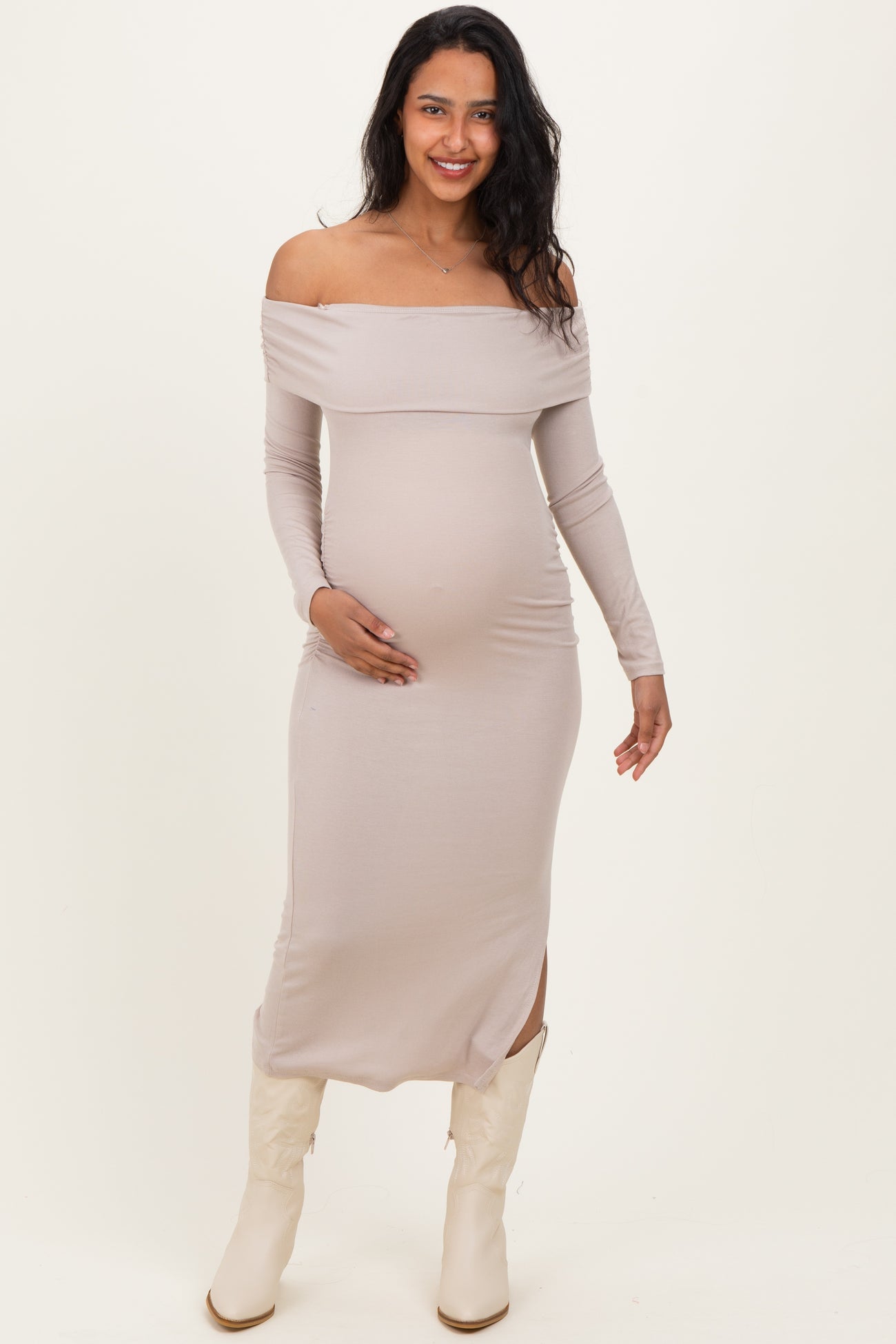 woman wearing a light taupe off-shoulder maternity dress with long sleeves and a visible baby bump
