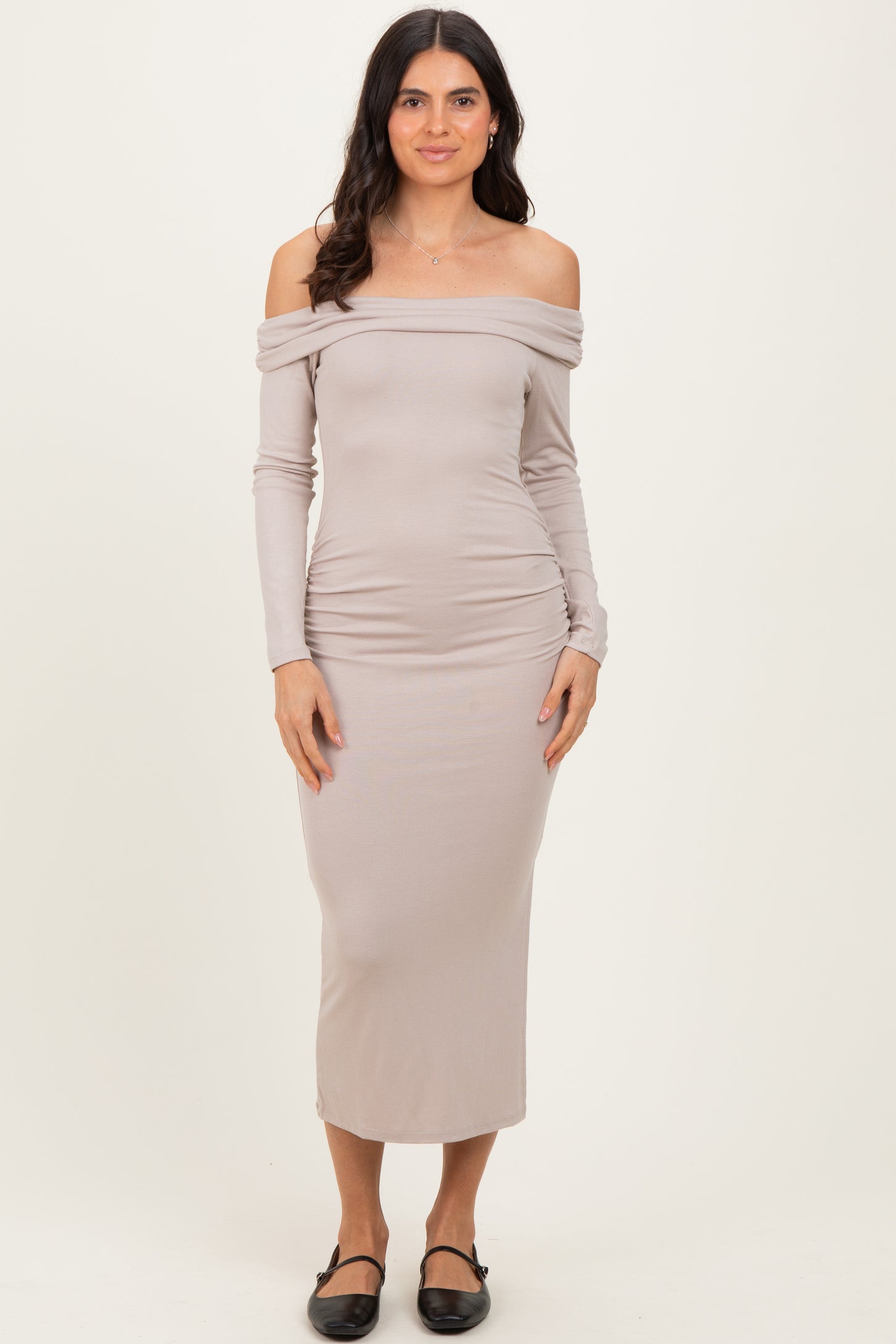 woman wearing a taupe off-the-shoulder long sleeve midi dress with ruched sides and black slip-on shoes