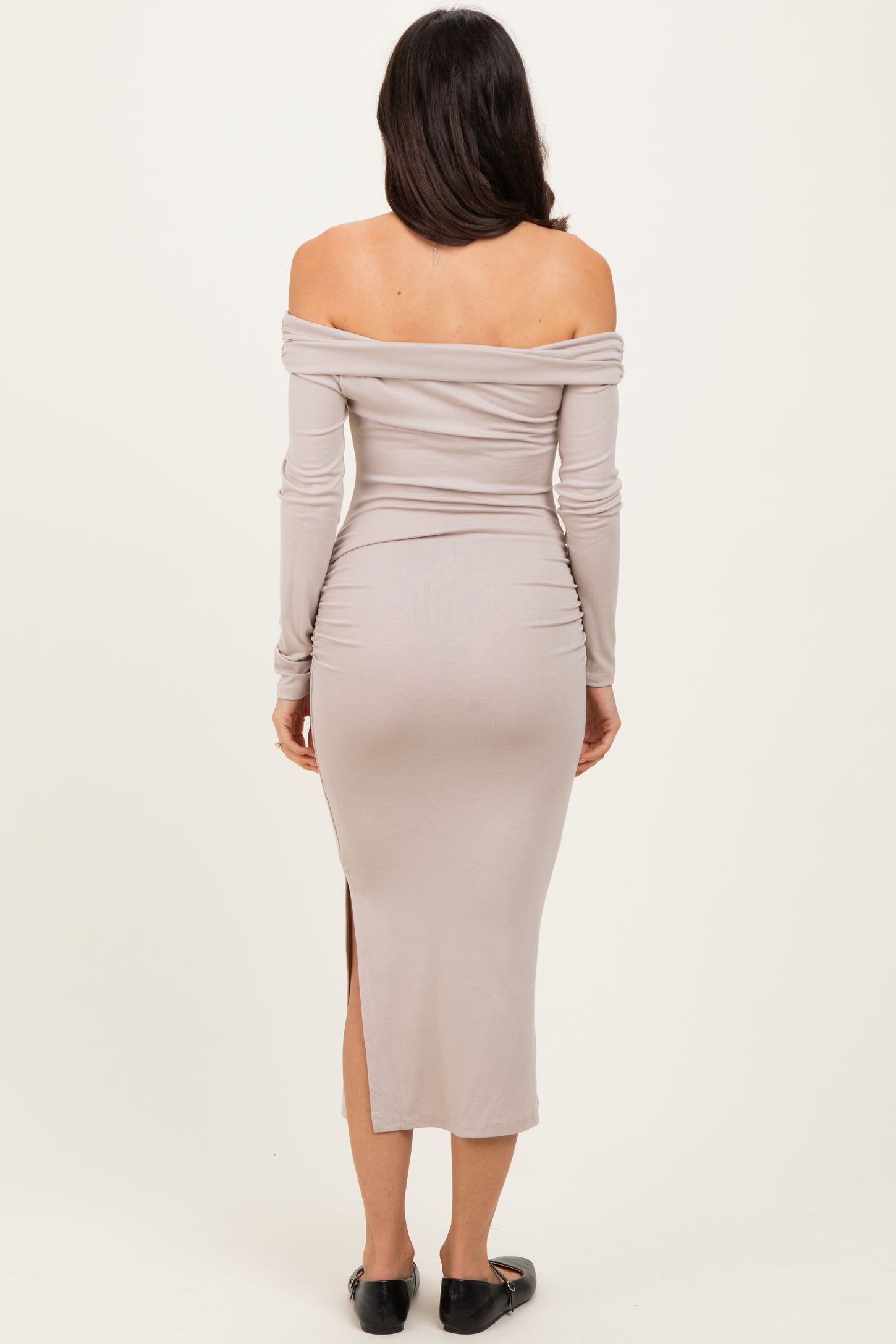woman wearing a beige off-the-shoulder midi dress with a slit and long sleeves, viewed from the back